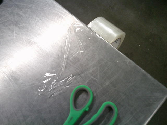 Roll of tape hanging off the edge of a table with scissors near it.